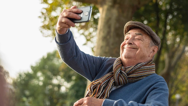 Ein Senior macht ein Selfie mit seinem Smartphone.