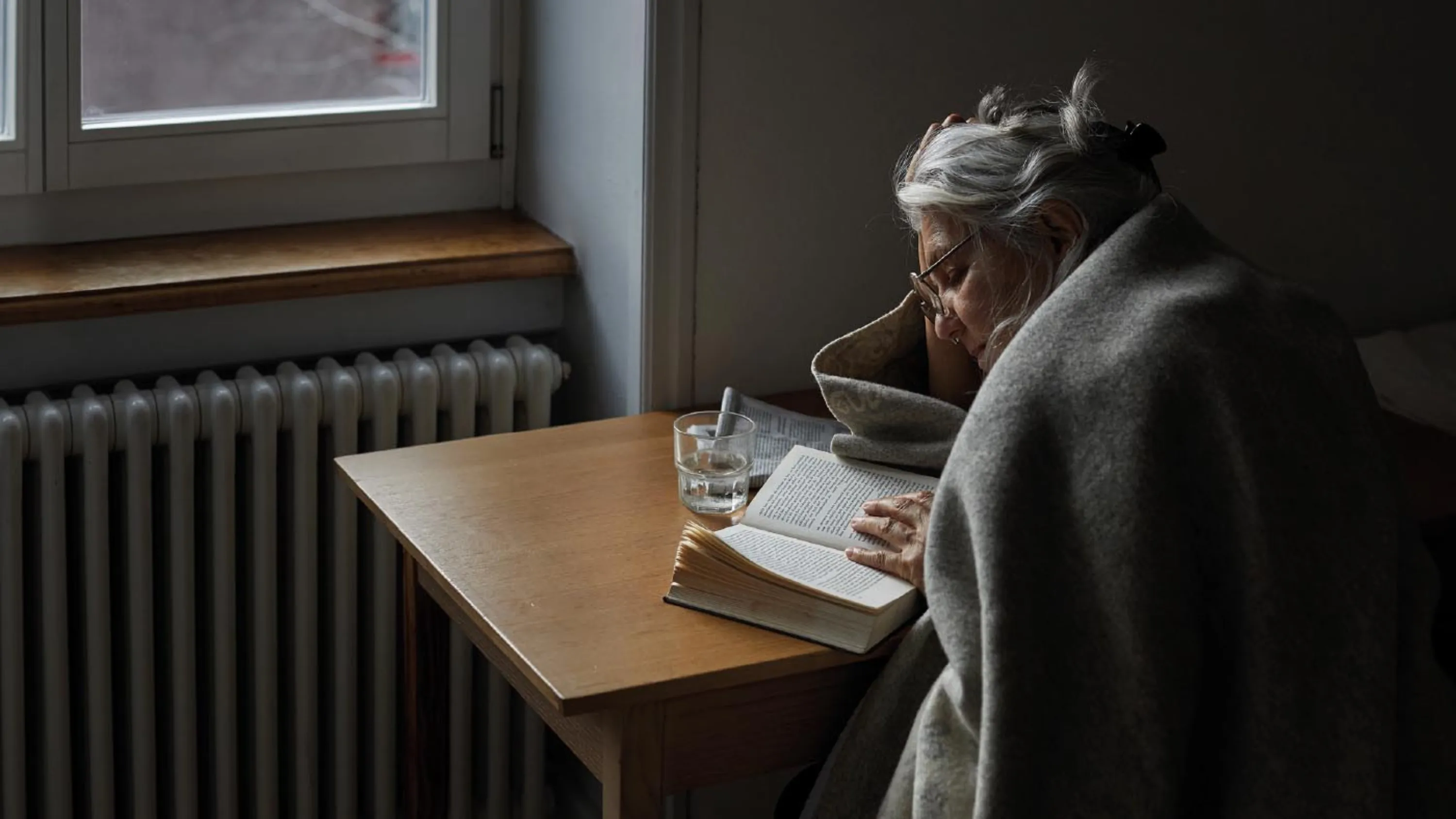 Donna anziana seduta a un tavolo che legge un libro.